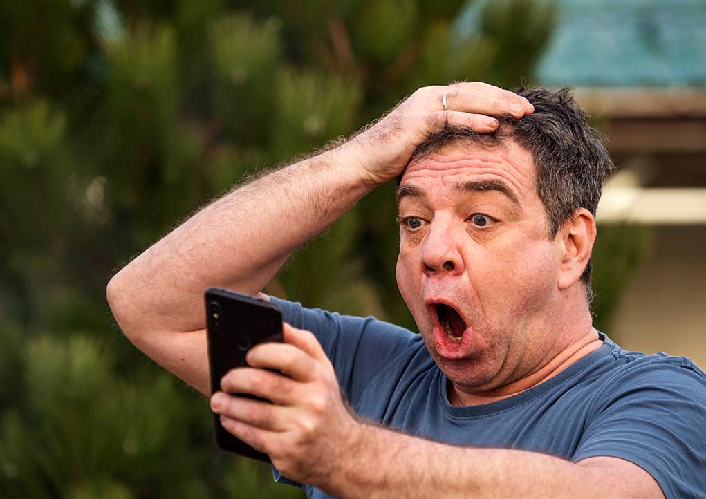 Man shocked while looking at his smartphone outside.