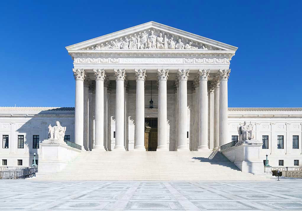 White columned building with stairs under a blue sky.