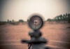 Rifle scope aiming at a distant silhouette target.