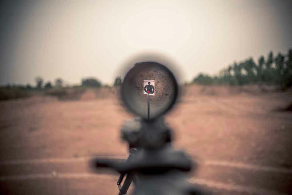 Rifle scope aiming at a distant silhouette target.