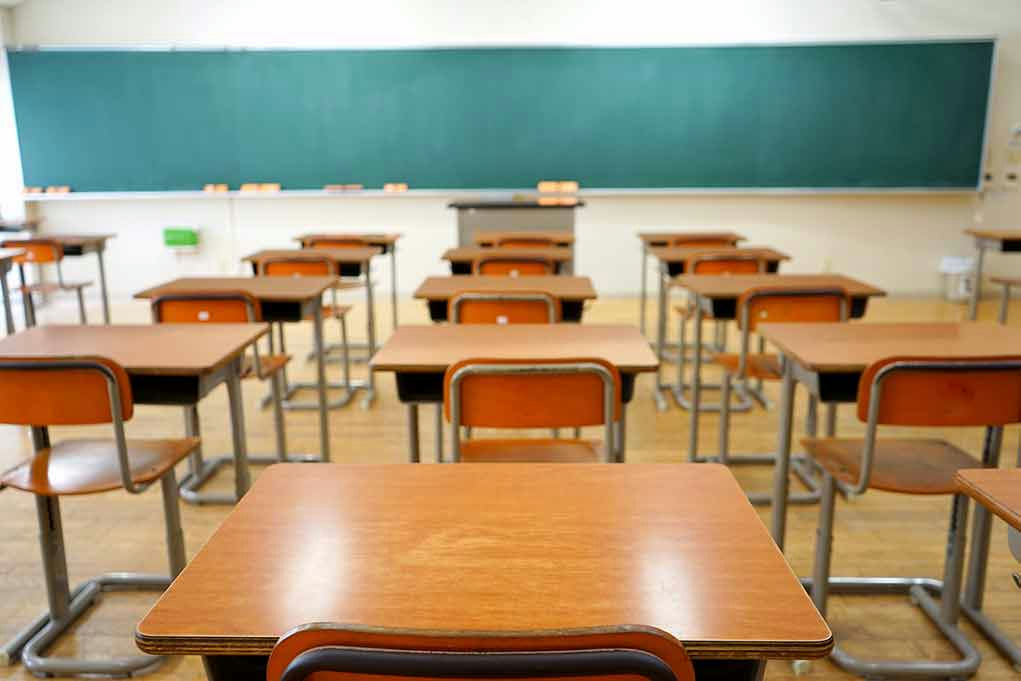 Empty classroom with wooden desks and chalkboard.