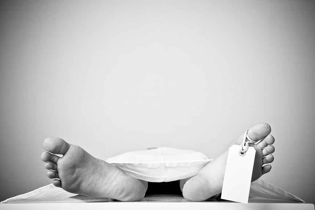 Bare feet with toe tag on body covered by sheet.