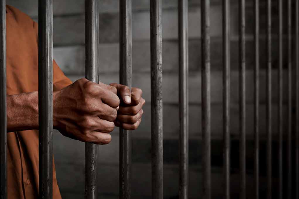 Hands gripping prison cell bars tightly.