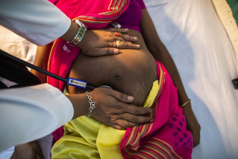A healthcare professional examining a pregnant woman's abdomen with a stethoscope