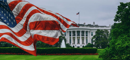 American flag waves before the White House on a cloudy day
