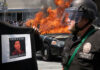 Protester holds George Floyd sign; police car burns.