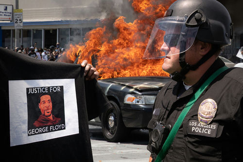 Protester holds George Floyd sign; police car burns.