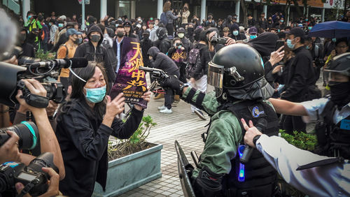 protester faces riot police amid crowd with cameras and masks