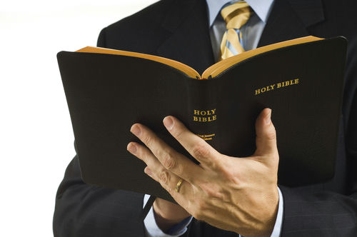 Man in suit holding an open Holy Bible.