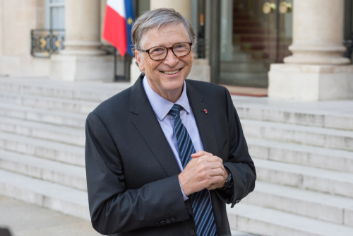 Man in suit outside building, flag in background.