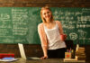 Woman holding mug standing in classroom with chalkboard.