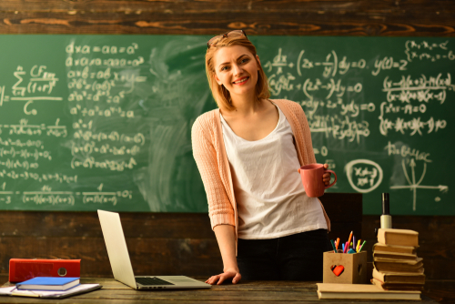 Woman holding mug standing in classroom with chalkboard.