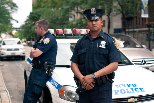 Two NYPD officers standing near a police car in an urban environment