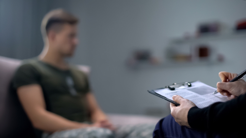 Therapist taking notes while talking with a young man.
