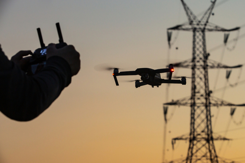 Hand operating drone near power lines at sunset.