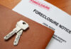 Keys on a foreclosure notice document and leather folder.