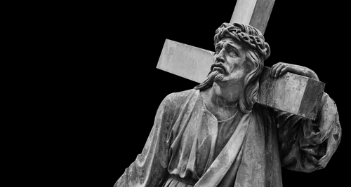 A black and white statue of Christ carrying a cross with a sorrowful expression