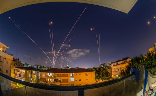 Night sky with missile defense system intercepting rockets above city.