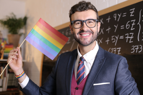 Man holding rainbow flag in classroom.