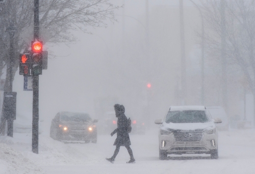Person crossing snowy street with cars in the background.