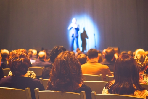 Audience watching a person on stage, under a spotlight.
