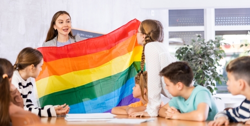 Teacher showing rainbow flag to children in classroom.