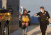 Man in yellow hoodie guided by masked security officer.