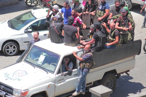 Men in military gear riding on a white pickup truck.