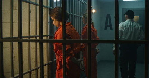 People in orange jumpsuits behind bars in a prison.