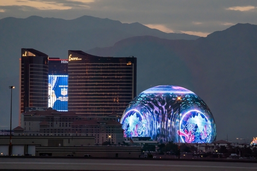 Las Vegas Sphere illuminated near hotels at dusk.