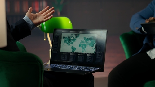 Person gesturing towards a laptop displaying a world map and data analytics