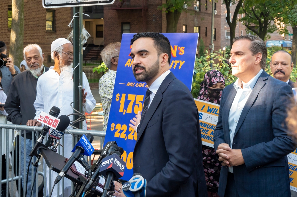 Man in suit speaks at outdoor press conference with microphones