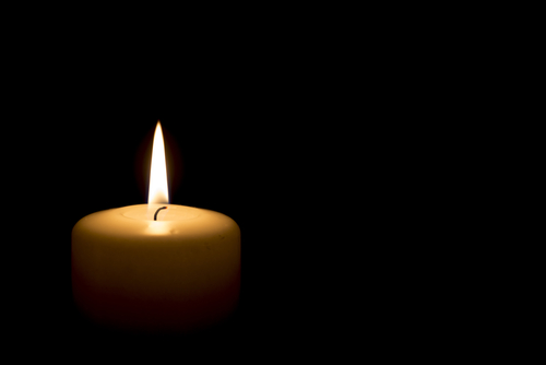 Single lit candle in darkness, flame glowing steadily.