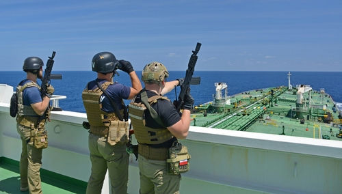 Armed security team on a ship deck overlooking a large tanker at sea