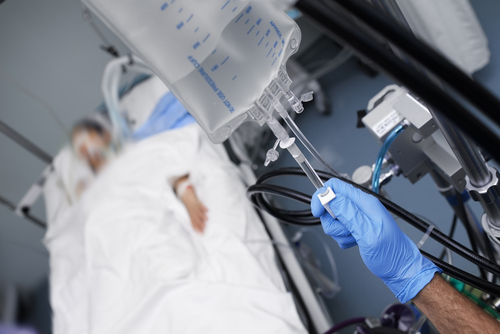 Person in hospital bed with IV drip being adjusted.