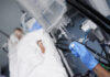 Person in hospital bed with IV drip being adjusted.