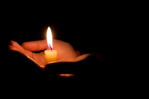 Hands holding a lit candle in darkness.